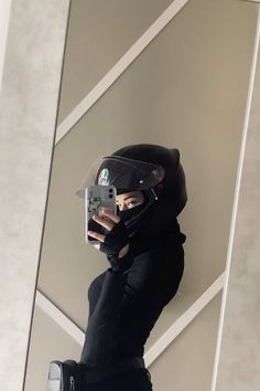 a person wearing a helmet and holding a cell phone up to their face while standing in front of a wall