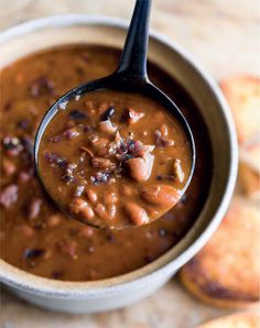 a spoon full of beans and bacon in a bowl with crackers on the side