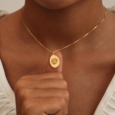 a woman wearing a gold necklace with a medallion on it