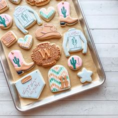 decorated cookies in the shape of cowboy hats and boots on a cookie sheet with white wood background