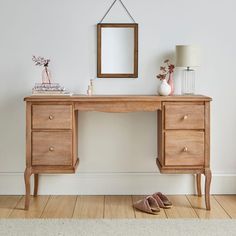 a wooden desk with two drawers and a mirror on it next to a pair of slippers