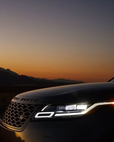 the front end of a car at sunset with mountains in the background