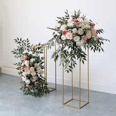 an arrangement of flowers and greenery on gold stands