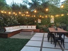 an outdoor patio with seating and lights strung over the back yard, surrounded by greenery