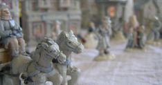 figurines of people riding on horses and carriages in front of buildings with snow covering the ground