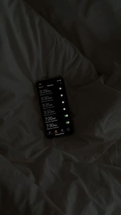 a cell phone sitting on top of a bed covered in white sheets with the time displayed