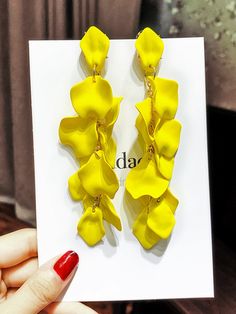 a pair of yellow flower earrings sitting on top of a white card next to a red nail