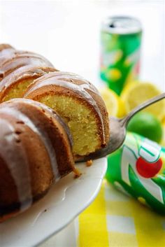 a bundt cake on a white plate with a fork in it next to cans of soda