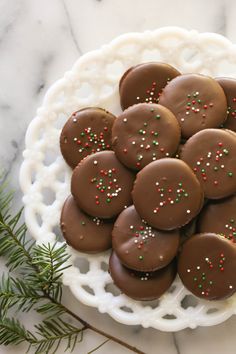 chocolate covered cookies with sprinkles on a white platter next to pine branches