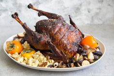 a whole chicken sitting on top of a white plate filled with vegetables and grains next to an orange