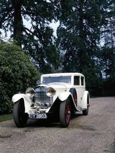 an old fashioned white car parked on the side of a road next to some trees