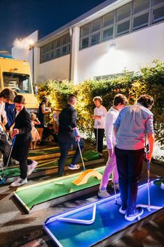 several people playing mini golf in front of a school building at night with lights on