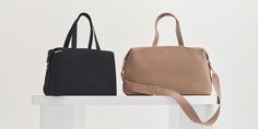 two purses sitting on top of a white table next to each other, one black and one tan