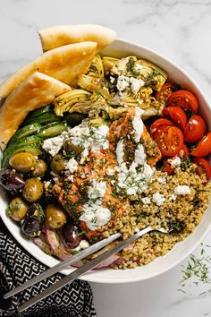 a white bowl filled with different types of food next to some bread and vegetables on a table