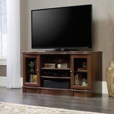 a large flat screen tv sitting on top of a wooden entertainment center next to a window