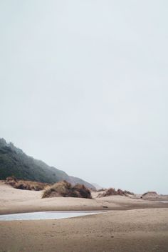 an empty beach with sand and hills in the background