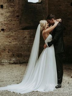 a bride and groom embracing each other in front of an old brick building with stone walls