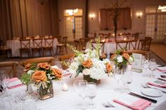 the table is set with white and orange flowers in vases, napkins, and silverware