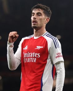 a close up of a soccer player wearing a red and white uniform with his fist in the air