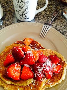 pancakes topped with strawberries and powdered sugar sit on a plate next to a coffee mug