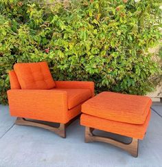 an orange chair and ottoman in front of some bushes