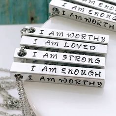 three necklaces with words on them sitting on top of a white table next to a chain