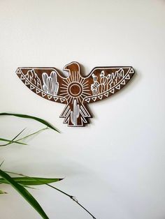 a wooden bird is hanging on the wall next to a potted plant and green leaves