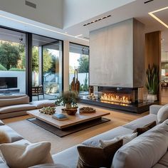 a large living room with couches and a fire place in the center, surrounded by glass doors