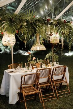 an outdoor dining area with palm trees and hanging lights above the table, surrounded by greenery