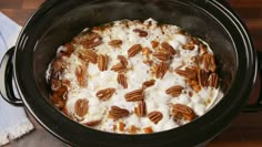 a crock pot filled with pudding and pecans on top of a wooden table