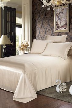 a white bed sitting in a bedroom next to a chandelier and lamp on a wooden floor