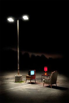 two chairs and a television sitting in the middle of a parking lot at night time