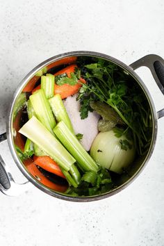 a pot filled with lots of vegetables on top of a white counter next to utensils