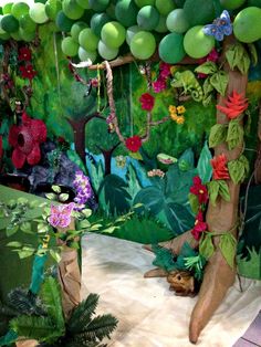 a room filled with lots of green balloons and flowers on the wall next to a tree