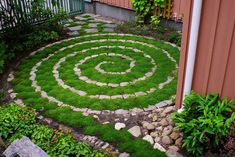 a garden with green grass and rocks in the shape of a spiral on top of it