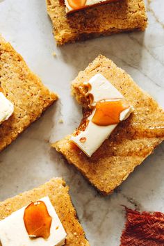 four square pieces of food on a marble surface with orange and white icing around them