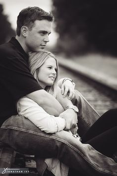 a man and woman sitting next to each other on train tracks with their arms around each other