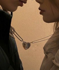 two young women standing next to each other with their faces close together, one has a heart shaped pendant on her neck