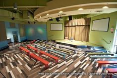 an empty lecture hall with benches and projector screen in the center, on top of multi - colored carpeted flooring