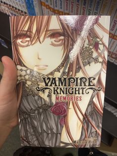 a person holding up a book in front of bookshelves with vampire knight memories written on it