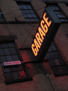 the neon sign is lit up on the side of the brick building that says garage