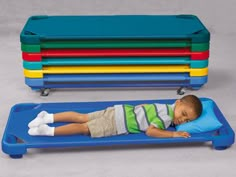 a young boy laying on top of a blue bed next to a stack of colorful plastic bins