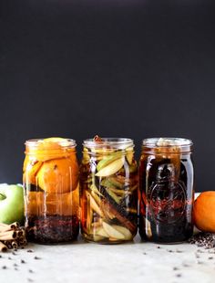 four jars filled with different types of food sitting next to an apple and other fruit