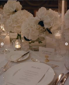 the table is set with white flowers and silverware