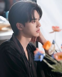 a young man sitting at a table with flowers in front of him and looking off to the side