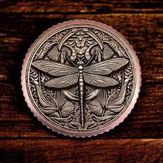 a metal plate with a dragonfly on it sitting on a wooden table next to flowers