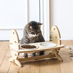 a cat sitting on top of a wooden chair eating out of it's food dish