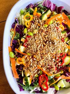 a salad with sesame seeds, carrots, and other vegetables in a white bowl on top of a wooden table