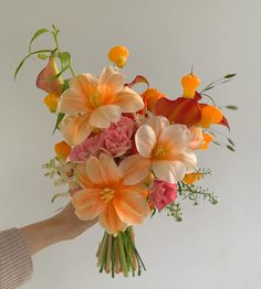 a person holding a bouquet of flowers in their hand with oranges and pinks