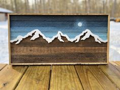 a wooden sign with mountains painted on it